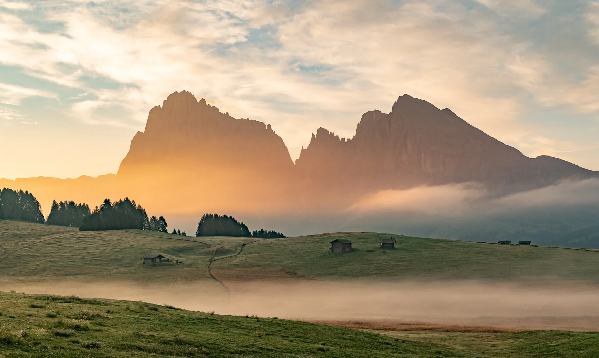 Sassolungo and Sasso Piatto above a layer of haze and dark meadow huts.
