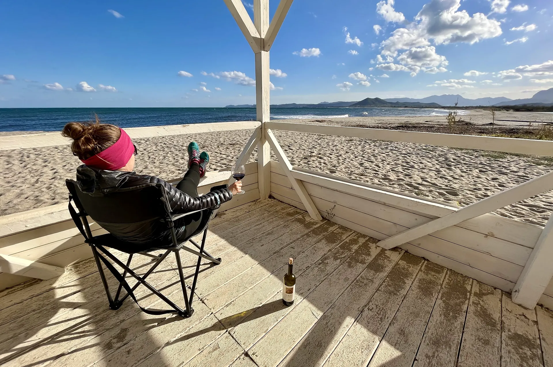 A woman sitting and drinking wine at empty beach bar at Spiaggia Orvile, Sardinia.