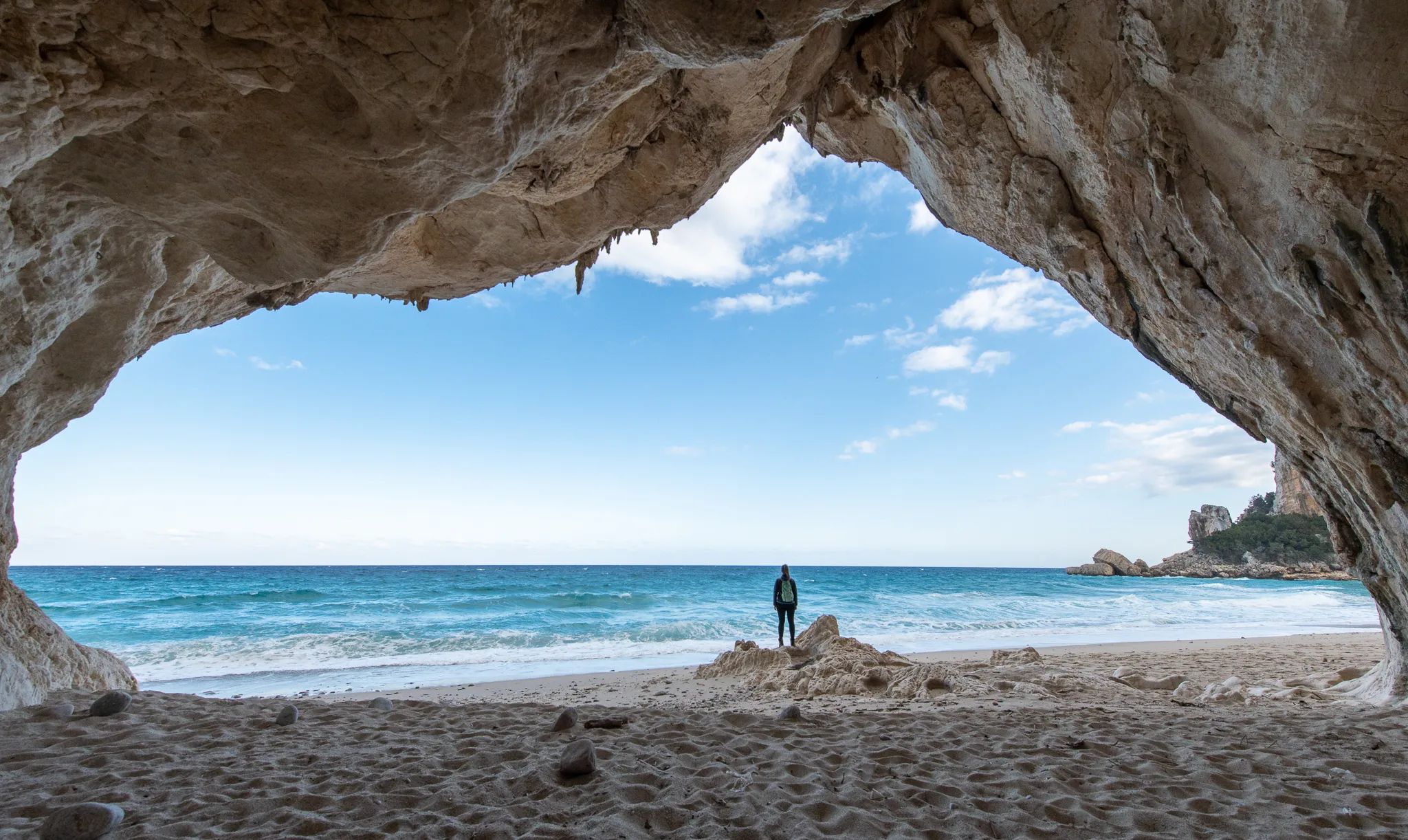 A woman standing in huge cave with blue see in the background. Cala Luna, Sardinia.